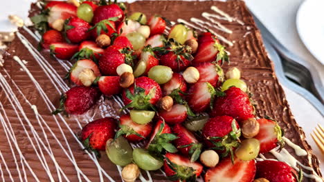 chocolate dessert topped with strawberries, grapes, hazelnuts, and white drizzle