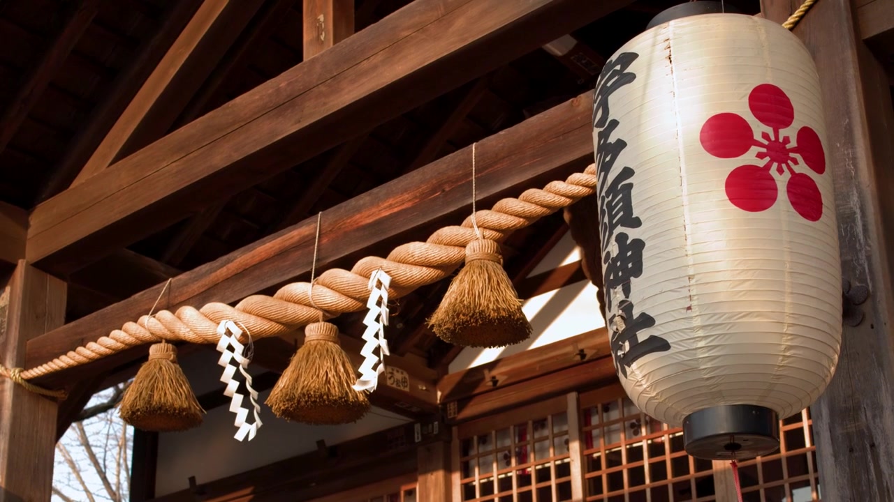 Nærbillede af en hvid papirlanterne og helligt reb på en Shinto-træbygning.