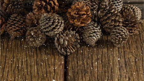 snow falling over multiple pine cones on wooden surface