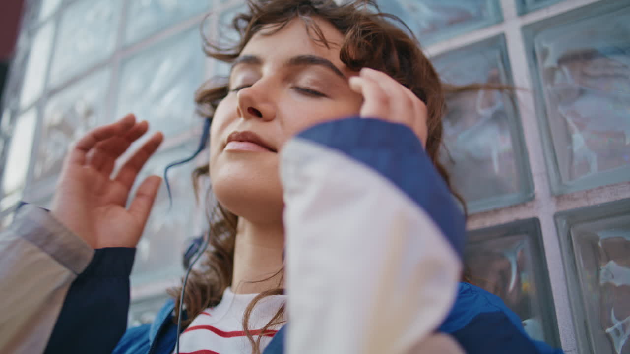 트렌디한 헤드폰 거리에서 휴식을 취하는 소녀 가까이. 음악을 듣는 곱슬한 여성