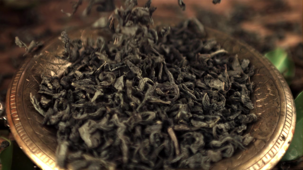 Dried Green Tea Leaves Falling into a Golden Bowl