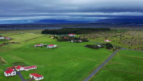 panoramic view of green meadow in gardakirkjugardur cemetery with dirt road, some houses and a church at the distant near reykjavik, iceland