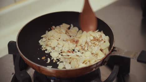 woman hand stirring almond nuts fried in a metal pan, on a gas cooking pan