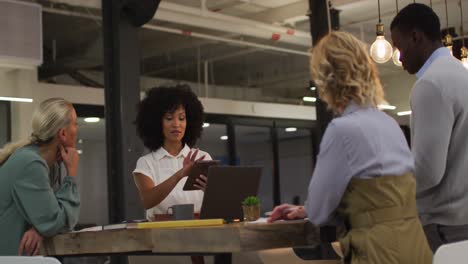 diverse group of business colleagues talking in a meeting room using tablet