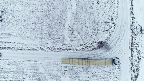 Long-truck-loaded-with-lumber-driving-on-snowy-rural-road