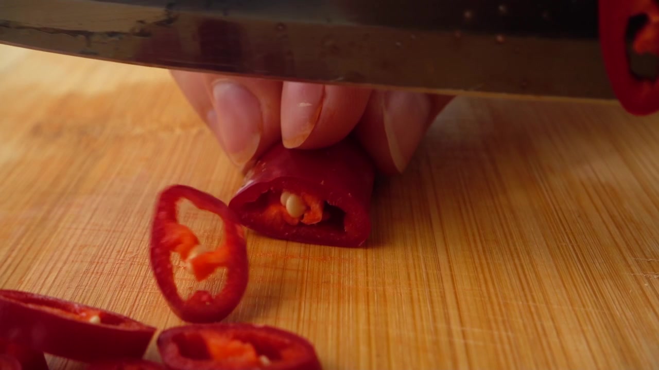 The cook cuts a bitter chilli pepper with a knife.
