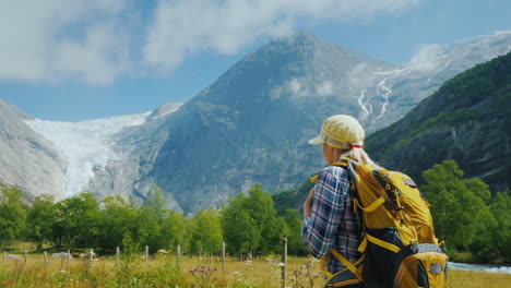 an active woman with a backpack walks against the backdrop of the mountains and the briksdal glacier