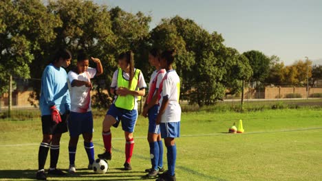 Female-soccer-team-discussing-tactics-on-soccer-field.-