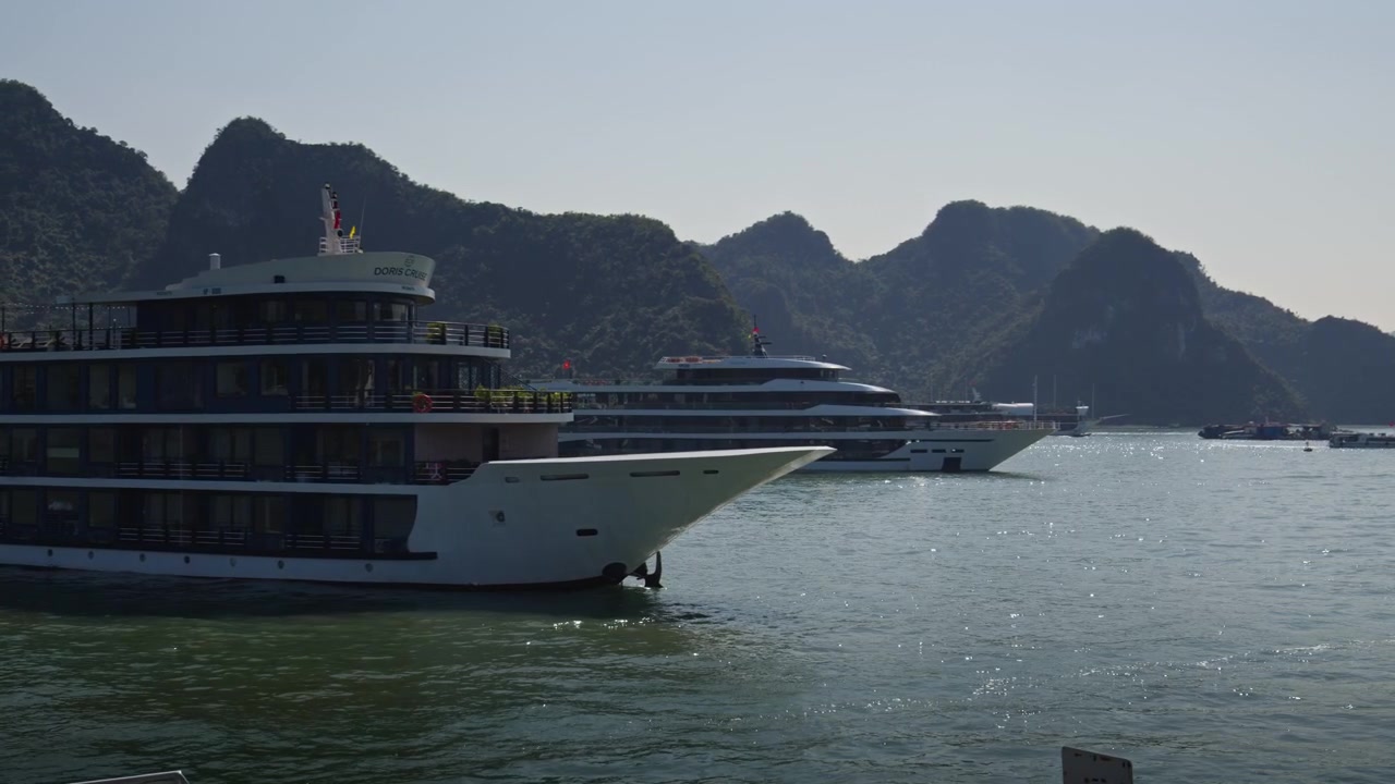 Ha Long, Quang Ninh, Vietnam. Luksus krydstogtskibe ankret i rolige bugtvande med kalkstensøer, der rejser sig i baggrunden. Tracking shot.