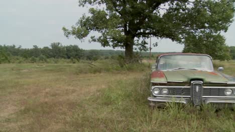 pan to an old abandoned ford edsel sitting in a field