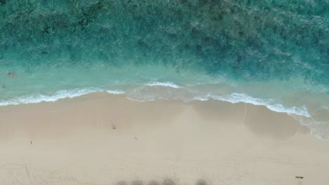 las imágenes de un dron muestran una playa golpeada por muchas pequeñas olas que se vuelven blancas y espumosas, y algunas personas nadan en el agua azul clara.