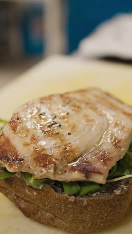 chef adding grilled swordfish on top of the vegetables preparing a burger