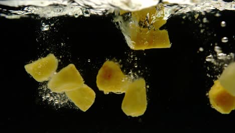 Super-slow-motion-of-fresh-mango-and-pineapple-falling-into-water-on-black-background