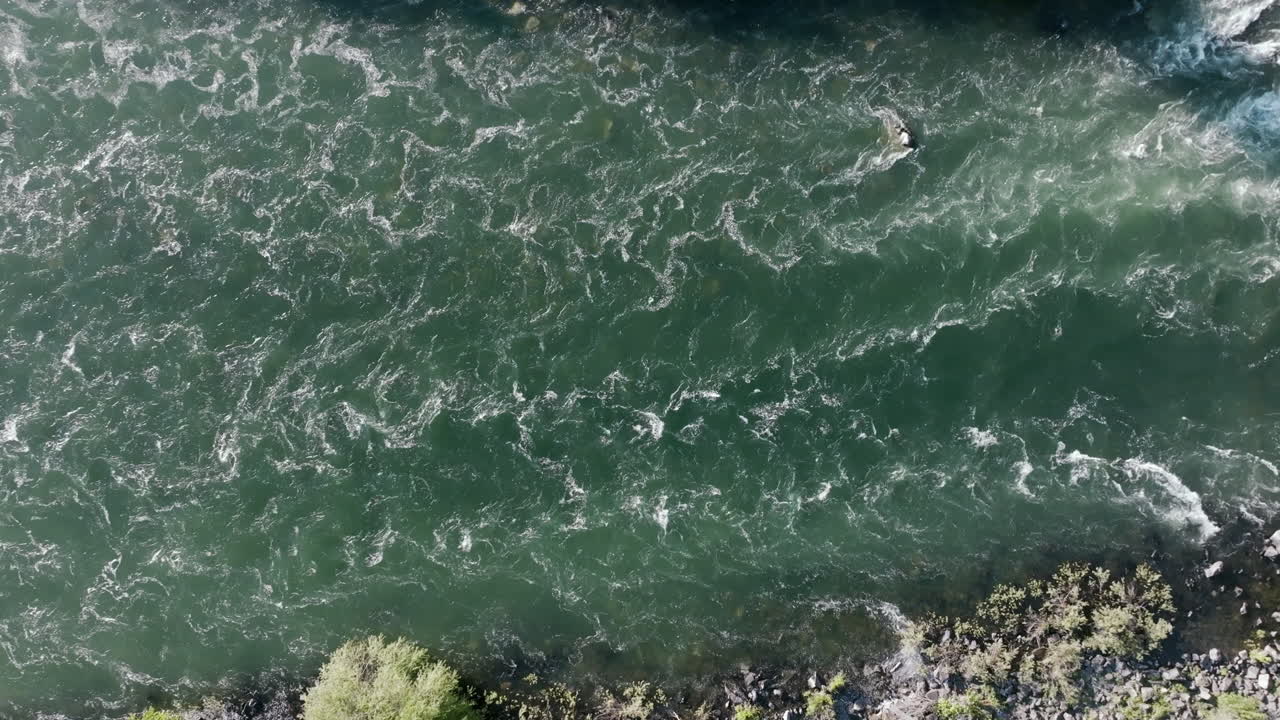 The river cuts between rocky shores and brush, full of visible movement. You can see swirls and eddies along the bank
