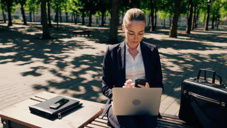 businesswoman working remotely on a laptop and smartphone in a park