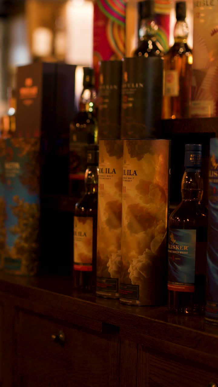 Bottiglie di whisky e confezioni su un bancone di legno, illuminazione interna calda, lenta panoramica della telecamera, un cliente entra.