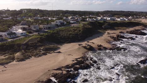 Drone-flying-along-rocky-coast-of-La-Pedrera-village-on-sunny-day,-Uruguay