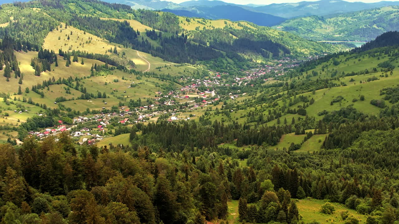Luftdronebilde av naturen i Karpatene i Romania ved solnedgang. Landsby som ligger i en dal, åser dekket med frodig skog