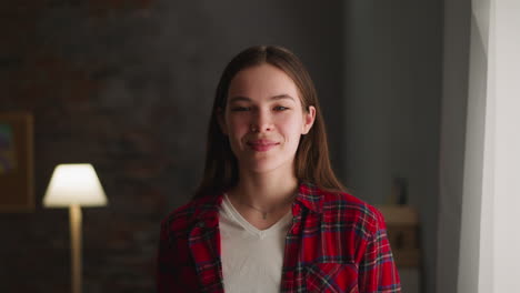 Positive-young-woman-in-casual-shirt-smiles-in-living-room