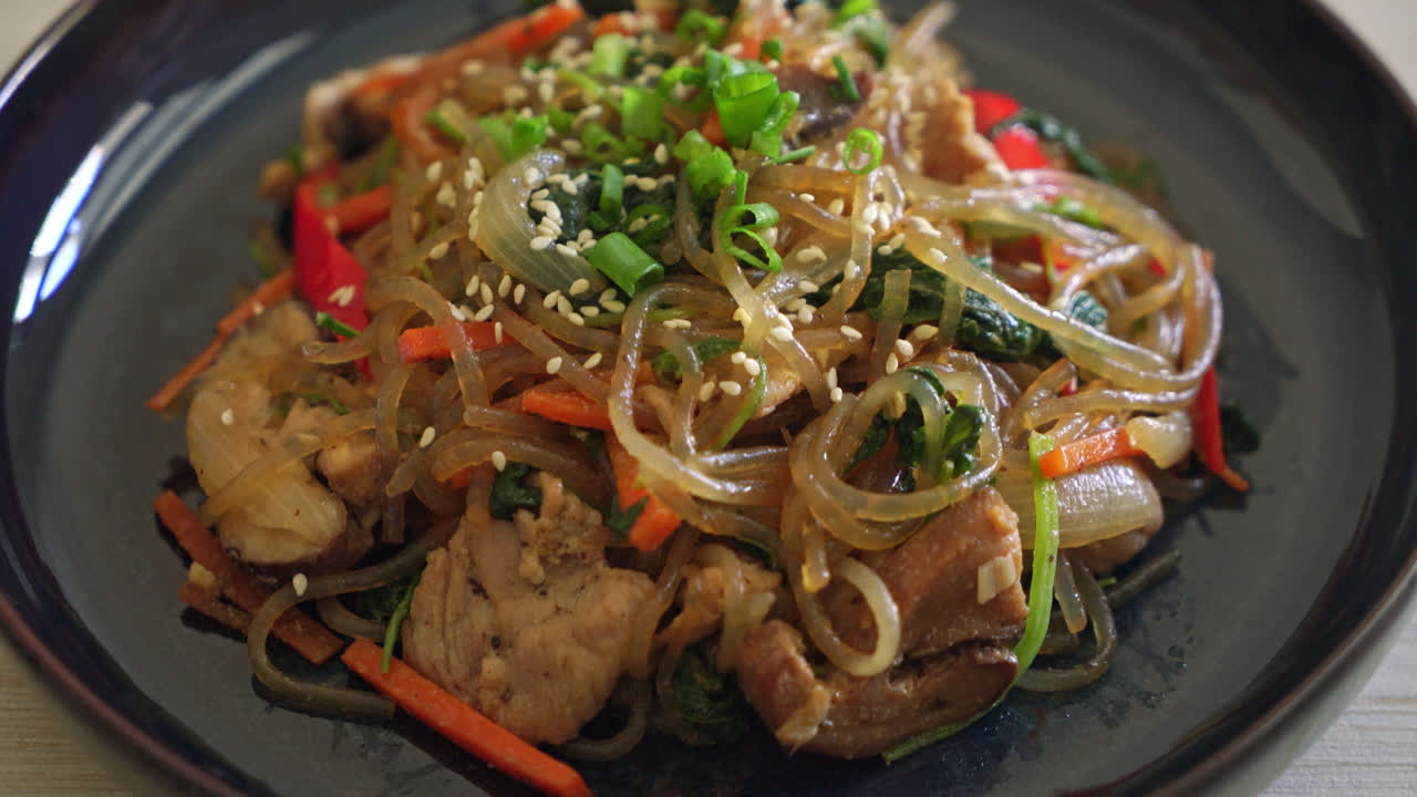 japchae o fideos vermicelli coreanos salteados con verduras y cerdo cubiertos con sésamo blanco - estilo de comida tradicional coreana