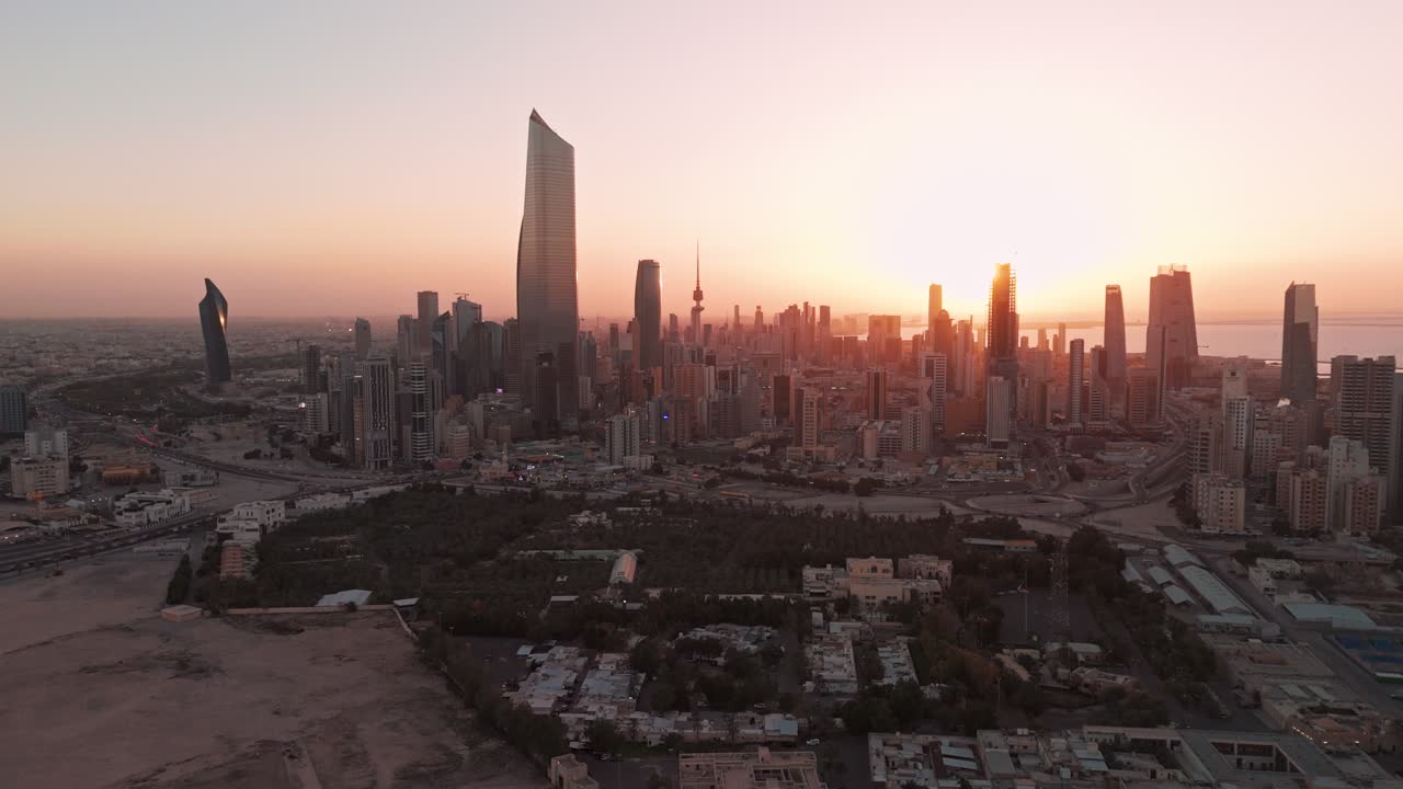 Ripresa aerea con drone di Kuwait City al tramonto, Al Hamra Tower e moderni grattacieli che brillano sull'autostrada costiera e sul lungomare del Golfo Arabico, paesaggio urbano cinematografico all'ora d'oro
