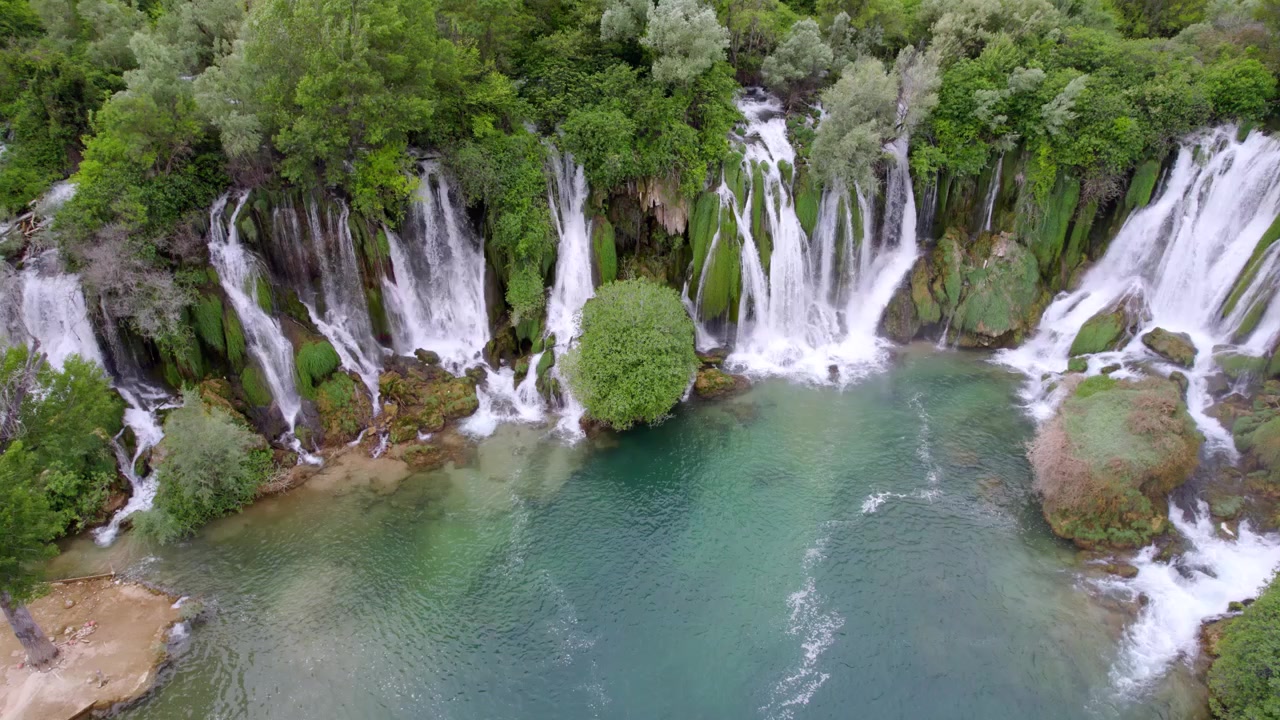 La Cascata di Kravica forma molteplici cascate bianche attorno a un bacino turchese e una foresta lussureggiante, con una panoramica aerea dall'alto