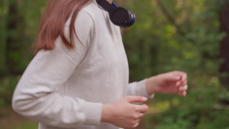 woman with headphones on neck jogs in park closeup. young lady starts day with cardio exercise to improve physical health in nature. healthy morning routine