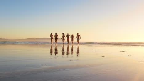 amigos corriendo a través de las olas al atardecer en vacaciones en la playa