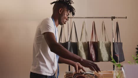 African-american-craftsman-with-dreadlocks-arranging-wallets-and-bags-in-leather-workshop-showroom