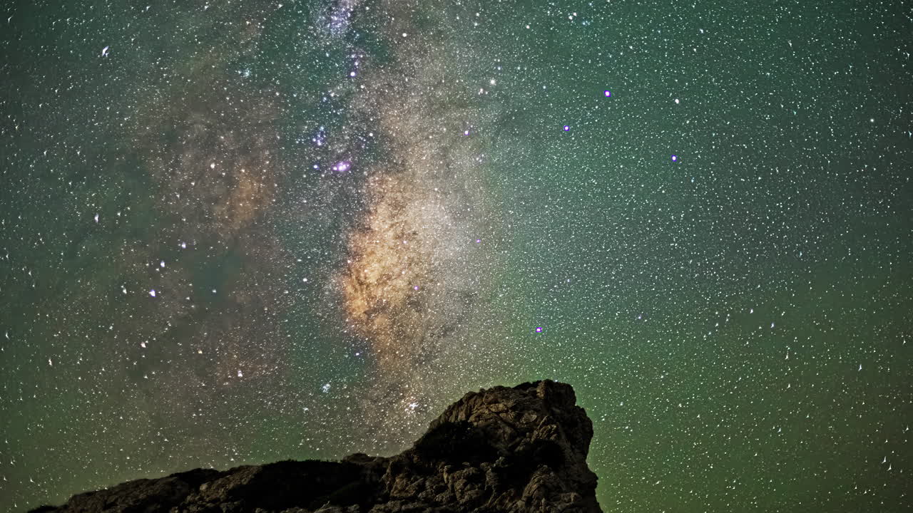 Timelapse Depicts the Milky Way Galaxy's Movement Across the Night Sky, Infusing Rocks Below with a Soft Emerald Radiance