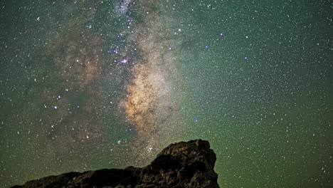 timelapse depicts the milky way galaxy's movement across the night sky, infusing rocks below with a soft emerald radiance