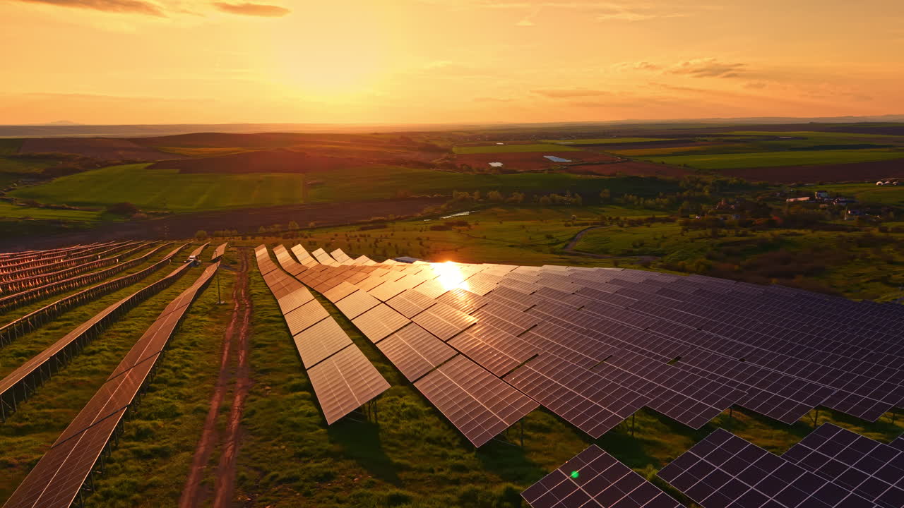 Solnedgang over solpaneler på en vedvarende energipark beliggende i en grøn dal med marker under en klar himmel i aftentimerne