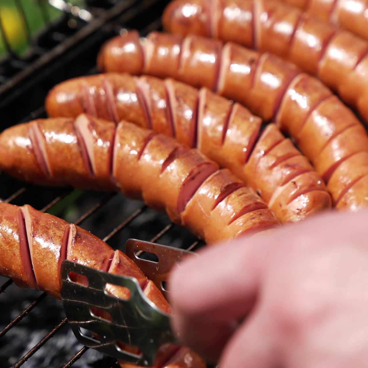 Sausages on a barbeque grill. Juicy sausages cooking over hot charcoal in smoke. Delicious food on a grill grate. Hand of chef turning sausages during cooking