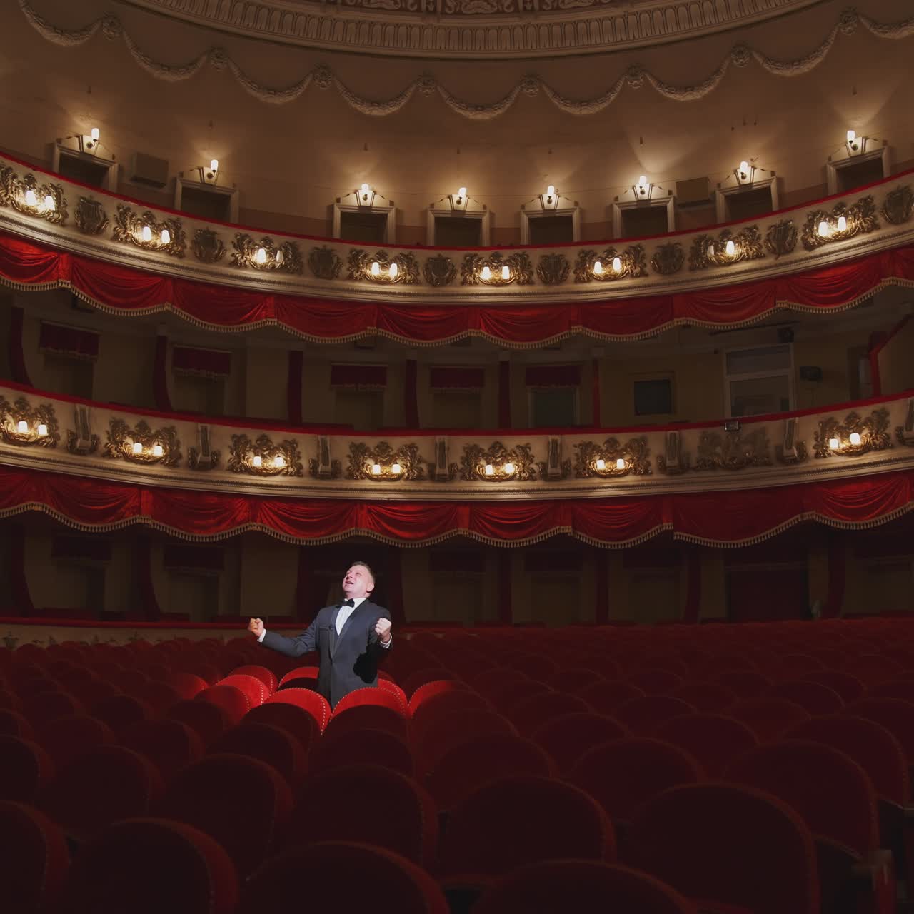 Actor among red seats in empty concert hall. Man in suit standing in beautiful large empty auditorium and talking something. Lockdown in the world.