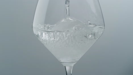 crystal clear liquid pouring over ice ball in wine glass