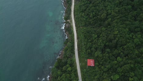 aerial view of a motorcycle driving along a tropical road, with dense jungle on one side and turquoise ocean on the other.