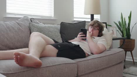 wide shot of young man on phone sitting on a couch