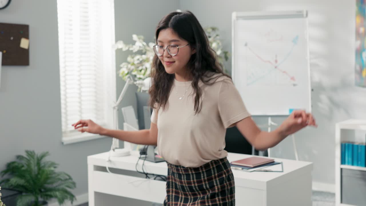 행복하고 만족한 사무실 직원은 승진을 얻었습니다. 그녀는 회사에서 책상 사이에 춤을 추고 있습니다. 한국의 아름다움을 가진 여자는 기쁜, 미소 짓고, 그녀의 의무에서 휴식을 취하면서 새로운 안무법을 연습합니다.