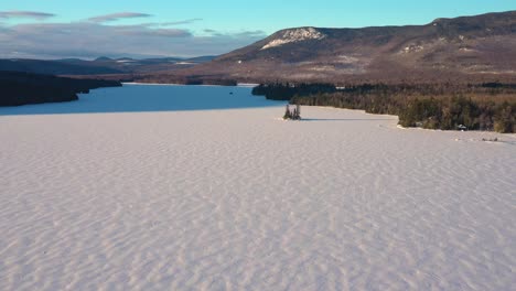 aerial push in towards small wooded island in a frozen northern lake in maine