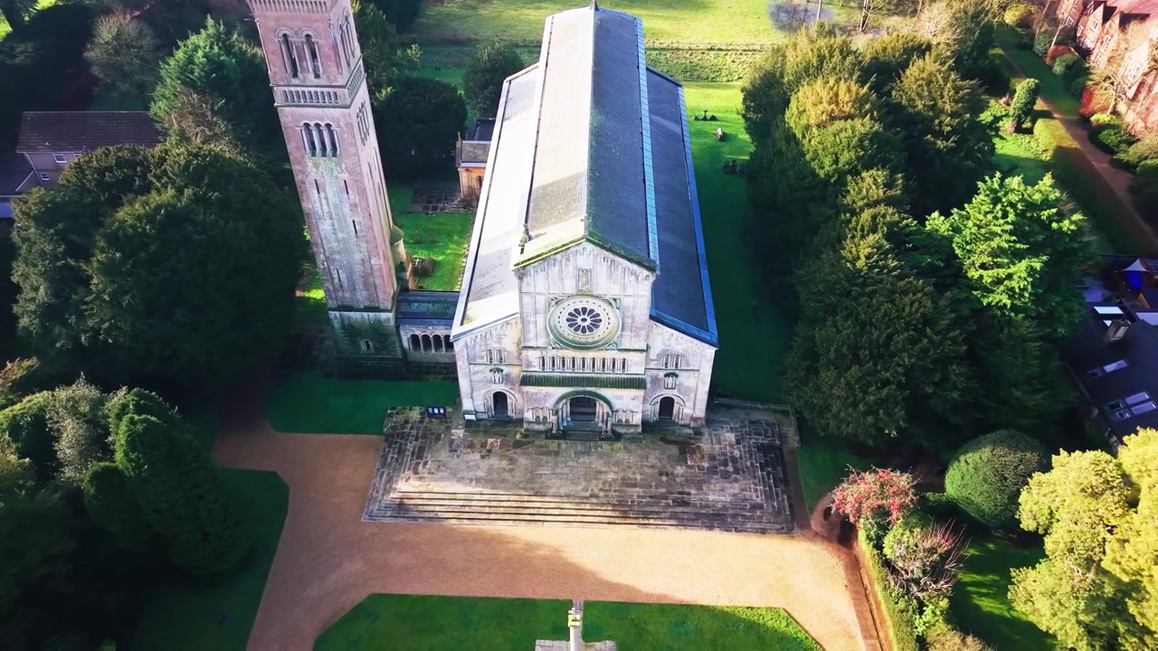 Imagens aéreas de drone de uma vista aproximada da fachada de uma igreja paroquial com uma rosácea com detalhes italianos e uma torre sineira separada.