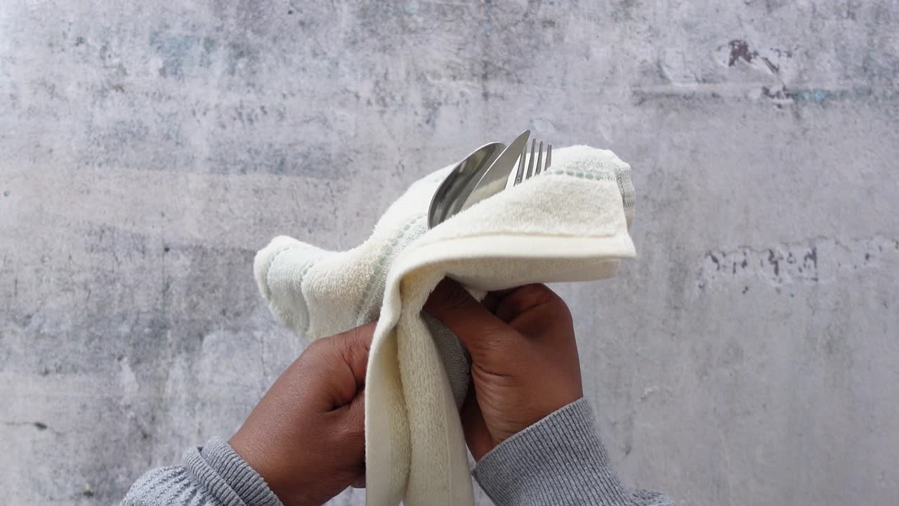 cerca de una mano que sostiene una toalla de plato con platos de plata en ella