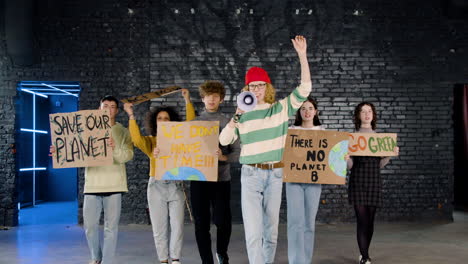 front view of young environmental activists with placards and megaphone walking towards camera and protesting against climate change inaction