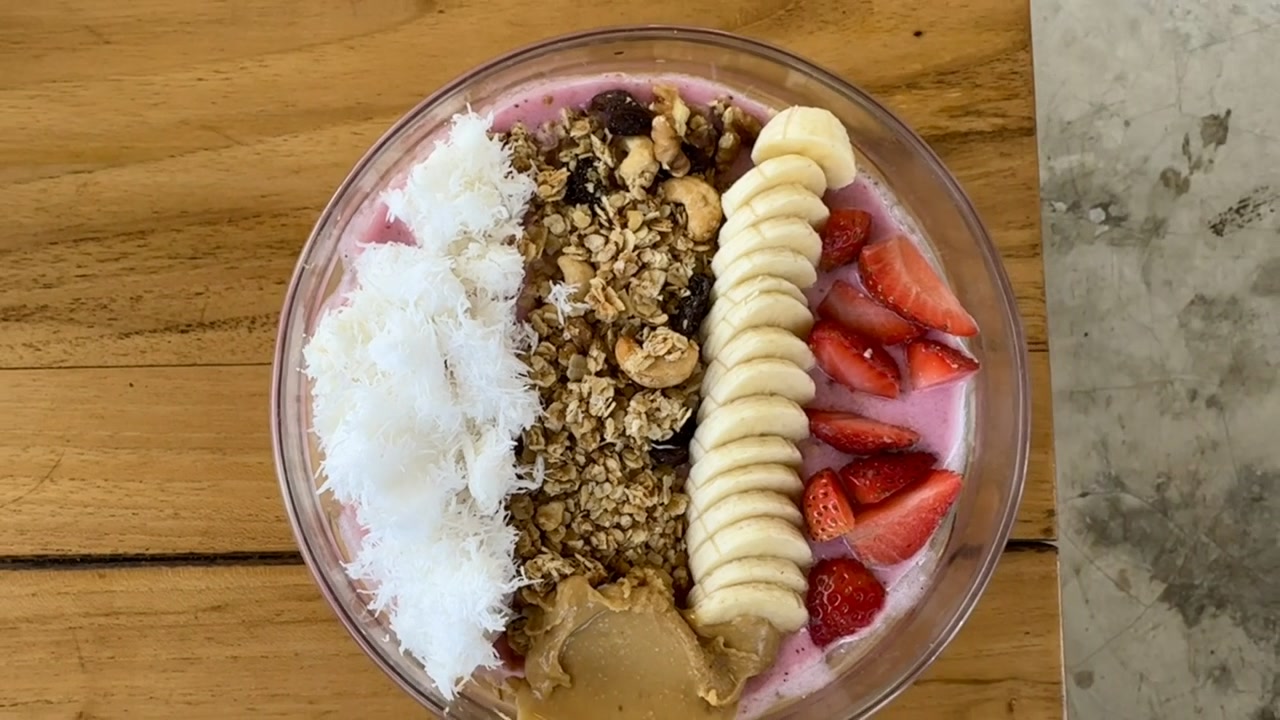 Kaunis smoothie-kulho, joka on valmistettu lohikäärmehedelmästä ja koristeltu tuoreella banaanilla, mansikoilla, maapähkinävoilla, kookoksella ja rapealla kotitekoisella granolalla.