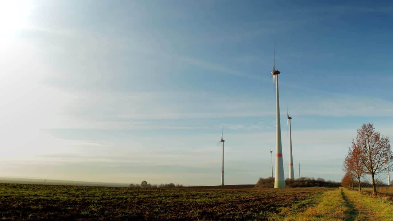 Time-lapse of a early morning as the sun rises on a small wind turbine farm with farmland in the foreground as it gets brighter and clouds moving by