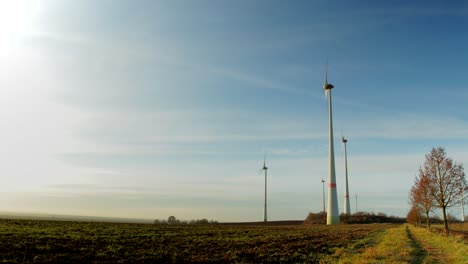 time-lapse of a early morning as the sun rises on a small wind turbine farm with farmland in the foreground as it gets brighter and clouds moving by