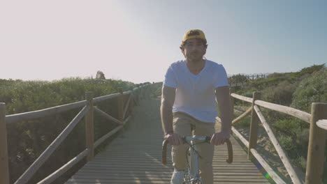 Männlicher-Radfahrer-Auf-Einem-Holzsteg-In-Richtung-Strand-2