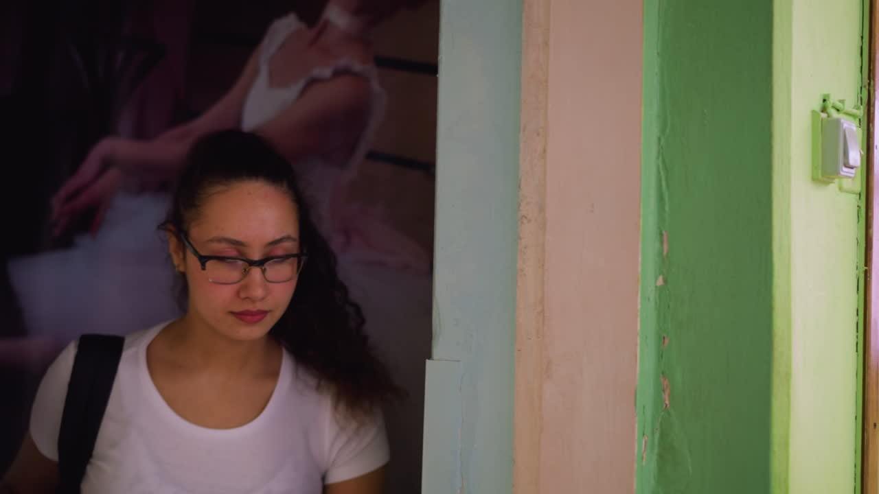 Close view of lady in white top and eyeglass gently stepping out through doorway while closing door calmly, green and beige wall background with visible white light switch