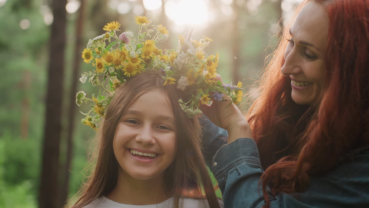 Lovely mom decorates smiling daughter hair with wild bouquets in warm sunlit forest, sharing gentle laughter surrounded by nature, expressing beauty, and emotional family connection outdoors