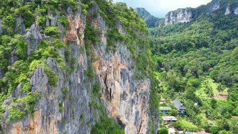 a tall rocky cliff covered in lush greenery with a small village nestled in the valley below, surrounded by mountains.