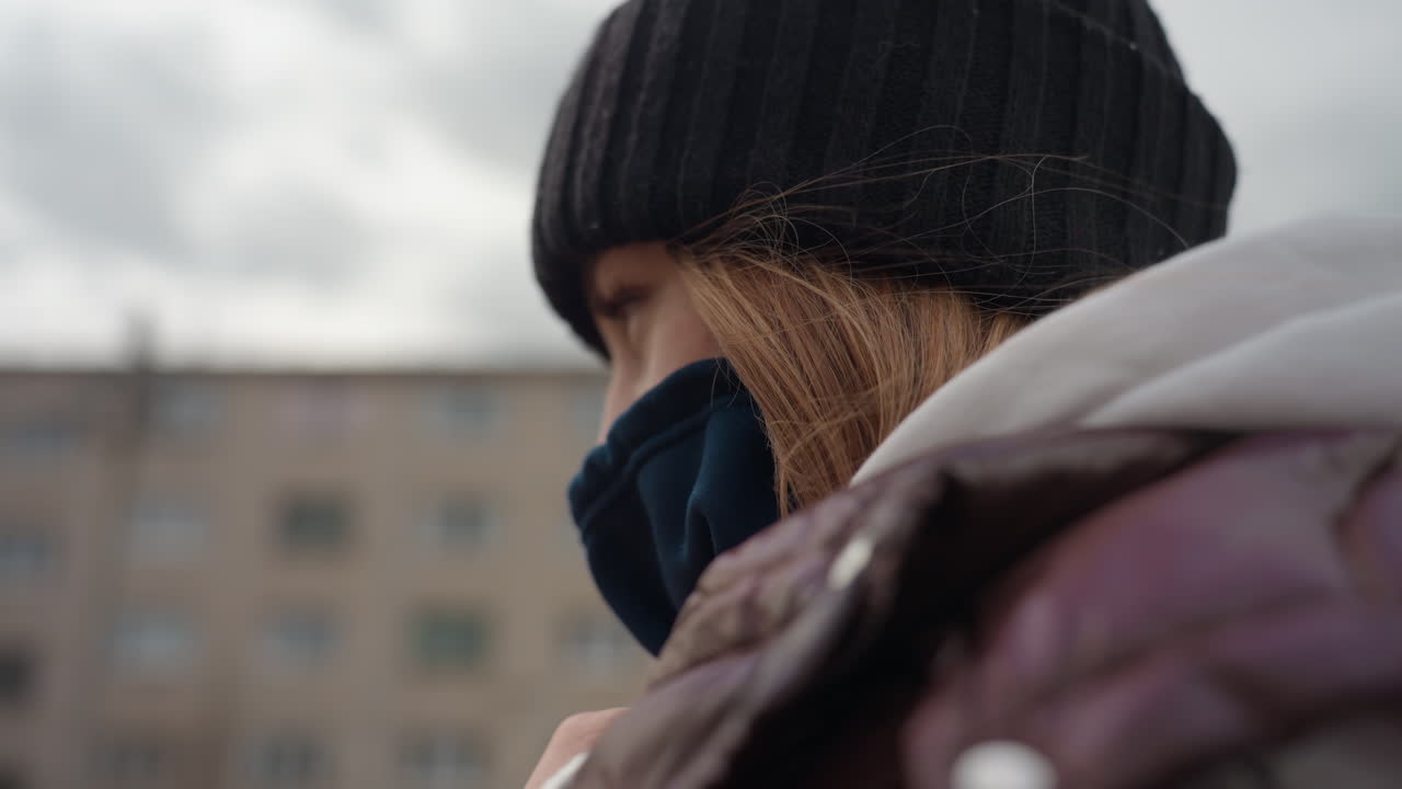 미소 짓는 젊은 여성, 마스크를 제대로 착용한 젊은 여성, 겨울 복장을 하고 자신감 있게 미소 짓는 여성, 흐린 하늘을 배경으로 보호 장비를 착용한 쾌활한 젊은 여성이 등장하는 도시 풍경